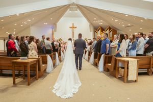 A wedding ceremony takes place in a modern church sanctuary with guests seated in wooden pews.