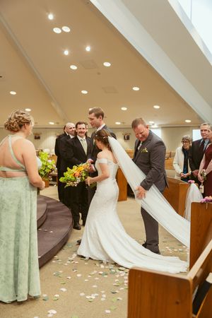 Elegant church wedding ceremony with bridesmaids in mint green dresses and scattered flower petals on the floor.