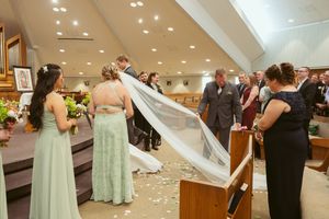 In a church decorated with flowers, guests gather around while a long white veil dramatically flows through the air.