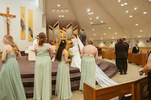 Bridesmaids in soft mint green dresses stand in line during a church wedding ceremony.