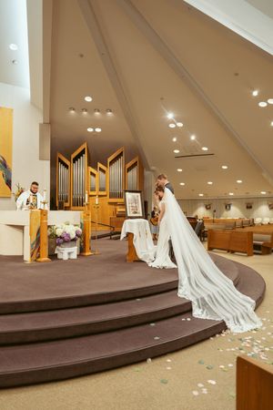 Church wedding ceremony in a modern chapel with an elegant pipe organ and scattered white flower petals on brown carpeted steps.