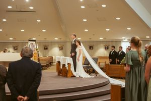 Wide angle view of a church sanctuary during a wedding ceremony with wooden pews and bright lighting.