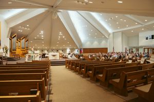 Panoramic view of a modern church sanctuary with wooden pews and angular white ceiling beams.