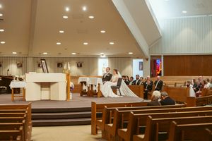 Modern church sanctuary interior with wooden pews and illuminated altar area under recessed lighting.