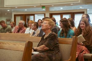 A congregation listens attentively during a church service while sitting in wooden pews.