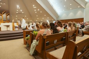 People seated in wooden pews during a church service under bright ceiling lights in a modern worship space.