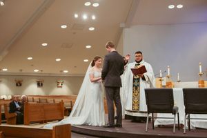 Wedding ceremony taking place at the altar of a modern church interior with recessed lighting overhead.