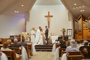 A wedding ceremony takes place in a Catholic church with a crucifix and organ pipes visible in the background.