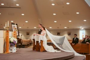 A flowing white wedding dress and veil drape dramatically across church altar steps during ceremony.