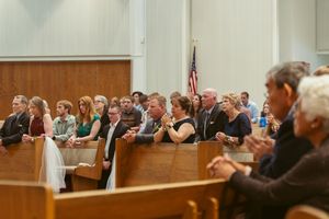 People seated in wooden pews during a formal church service or ceremony as seen from a side angle.