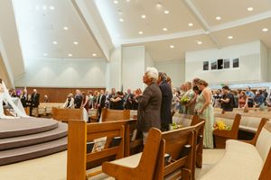 Interior view of a modern synagogue or temple showing rows of wooden pews and illuminated ceiling during a gathering.