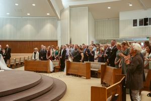 People stand in a courtroom setting with recessed lighting and wood paneling during a formal legal proceeding.