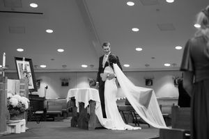 A bride in a flowing white wedding dress trails behind during a final wedding dress fitting in a bridal boutique.
