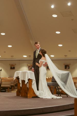 Wedding couple shares a dramatic moment with flowing white veil in a church sanctuary with wooden pews and organ pipes.