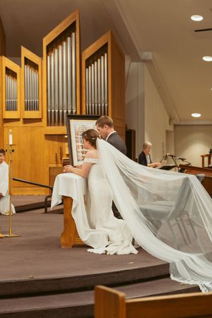 Elegant white wedding veil flows across raised church platform near wooden organ pipes during ceremony.