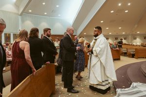 Religious ceremony taking place in a modern church interior with wooden pews and people gathered in formal attire.