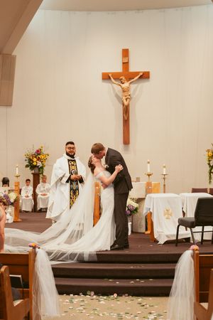 A wedding ceremony at a church altar with a wooden crucifix mounted on the white wall behind.