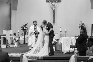 Black and white photograph of wedding ceremony in church sanctuary with decorative floral arrangements.