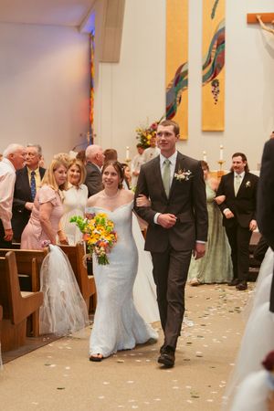 A joyful wedding ceremony recessional with yellow sunflowers and scattered petals in a modern church setting.