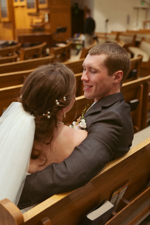 Newlyweds share an intimate moment while seated in a wooden church pew.