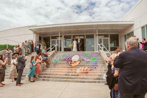 Wedding guests gather outside modern building entrance with painted sidewalk decorations.