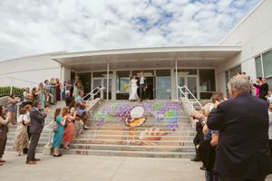 Crowd gathering outside a modern white building with artistic decorations on concrete steps under cloudy skies.