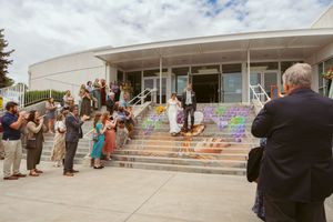 People assembled on outdoor concrete steps of a modern building with colorful artwork and decorative elements.