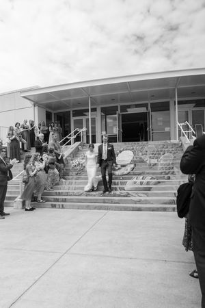 Wedding guests gather on outdoor concrete steps of a modern building on an overcast day.