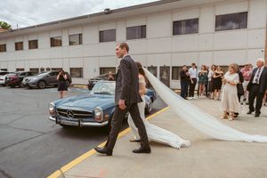 A classic blue Mercedes-Benz parked outside as a couple exits through flowing white fabric.