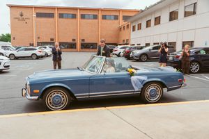 A classic blue Mercedes convertible parked outside a brick building.