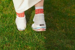 Close-up of white high-top sneakers with red patterned socks and 'WIFE' text on heel, standing on grass.