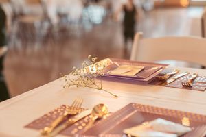 Close-up of elegant table setting with gold cutlery, documents and delicate floral accents in warm lighting.