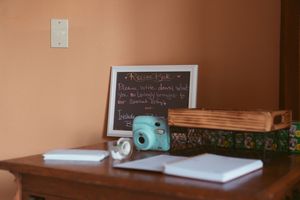 A mint green Instax camera sits on a wooden desk next to a chalkboard and notebooks.
