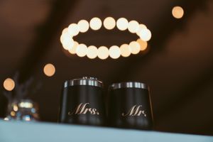 Mr and Mrs coffee tumblers with a circular light bokeh effect glowing above them against a dark background.
