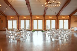 Elegant wedding ceremony venue with white chairs arranged in rows under rustic wooden beams and decorative chandeliers.