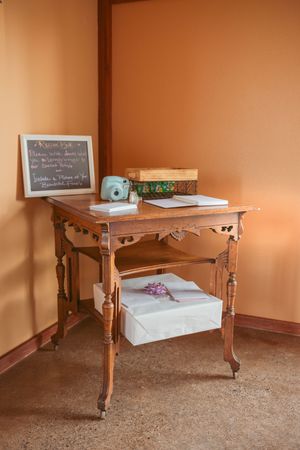 Vintage wooden side table with chalkboard and decorative items against orange wall at wedding venue setup.