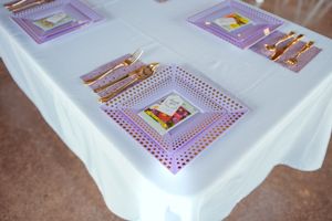 White table settings with purple-themed place cards displayed at a formal event.