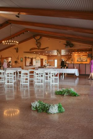 Rustic wedding reception hall with white chairs, exposed beams, chandeliers and floral arrangements.