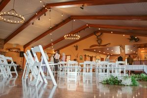Large event venue with exposed wooden beams, white chairs, and string lighting creates an elegant atmosphere.