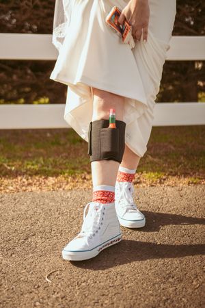 Bride wearing white sneakers with red socks and garter belt visible under wedding dress.