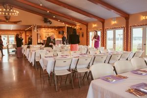 Elegant banquet hall with rows of white-clothed tables, exposed beams, and warm lighting for a wedding reception.