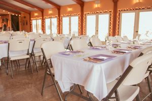 Wedding reception venue set with white tablecloths and folding chairs in warm-lit room.