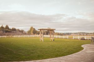 Panoramic view of a grassy field with white fences and pergola under cloudy skies.