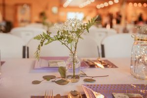 Table settings with purple accents, mason jars, and delicate floral arrangements at a rustic reception.