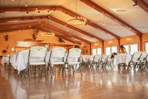 Empty wedding reception venue with vaulted ceilings, string lights, and rows of tables set with white linens.