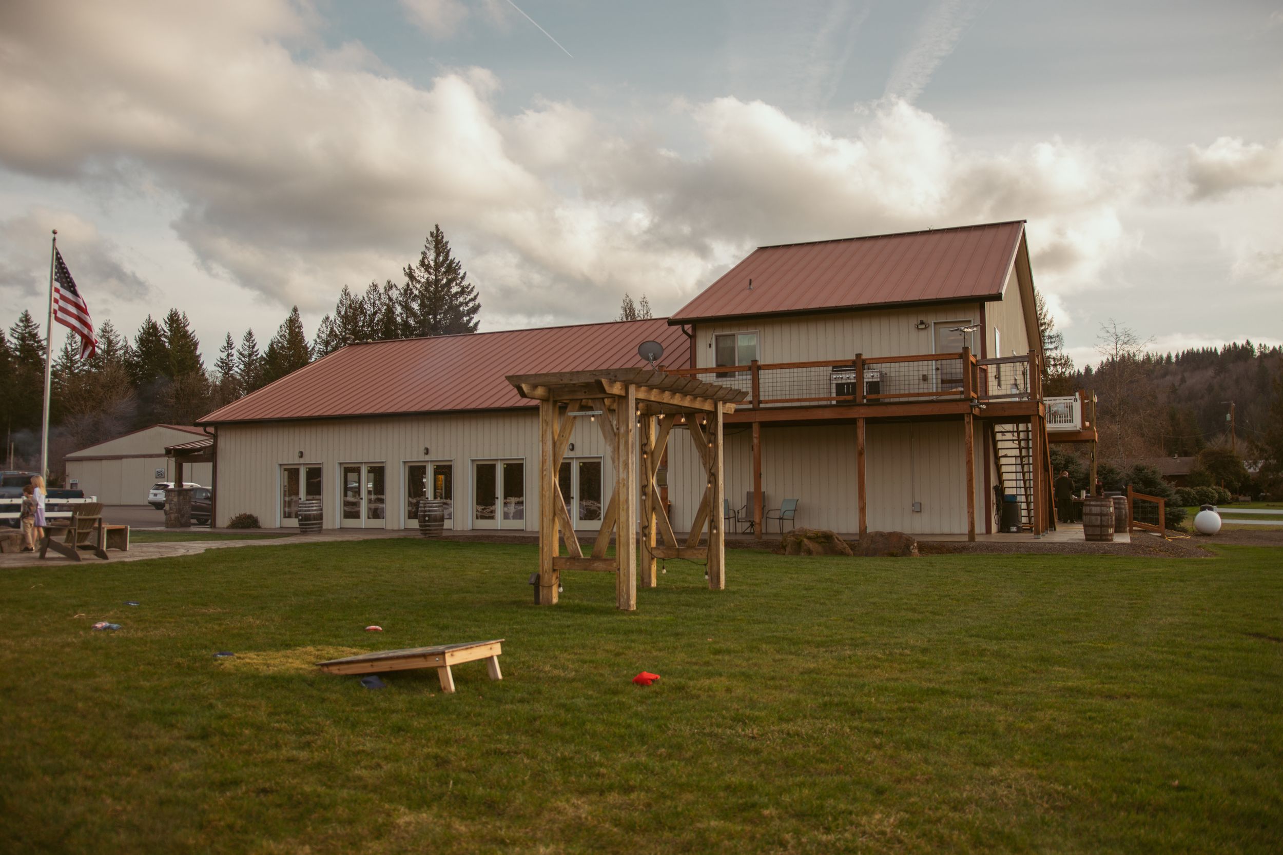 A panoramic view of a church building with green lawn and flag pole under cloudy skies.