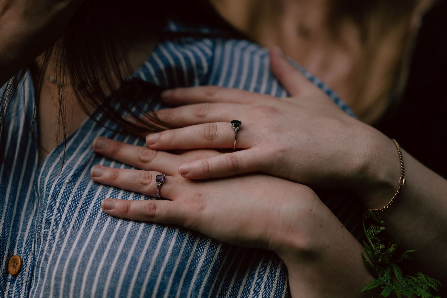 Close-up of hands wearing engagement rings against a striped blue and white shirt background.
