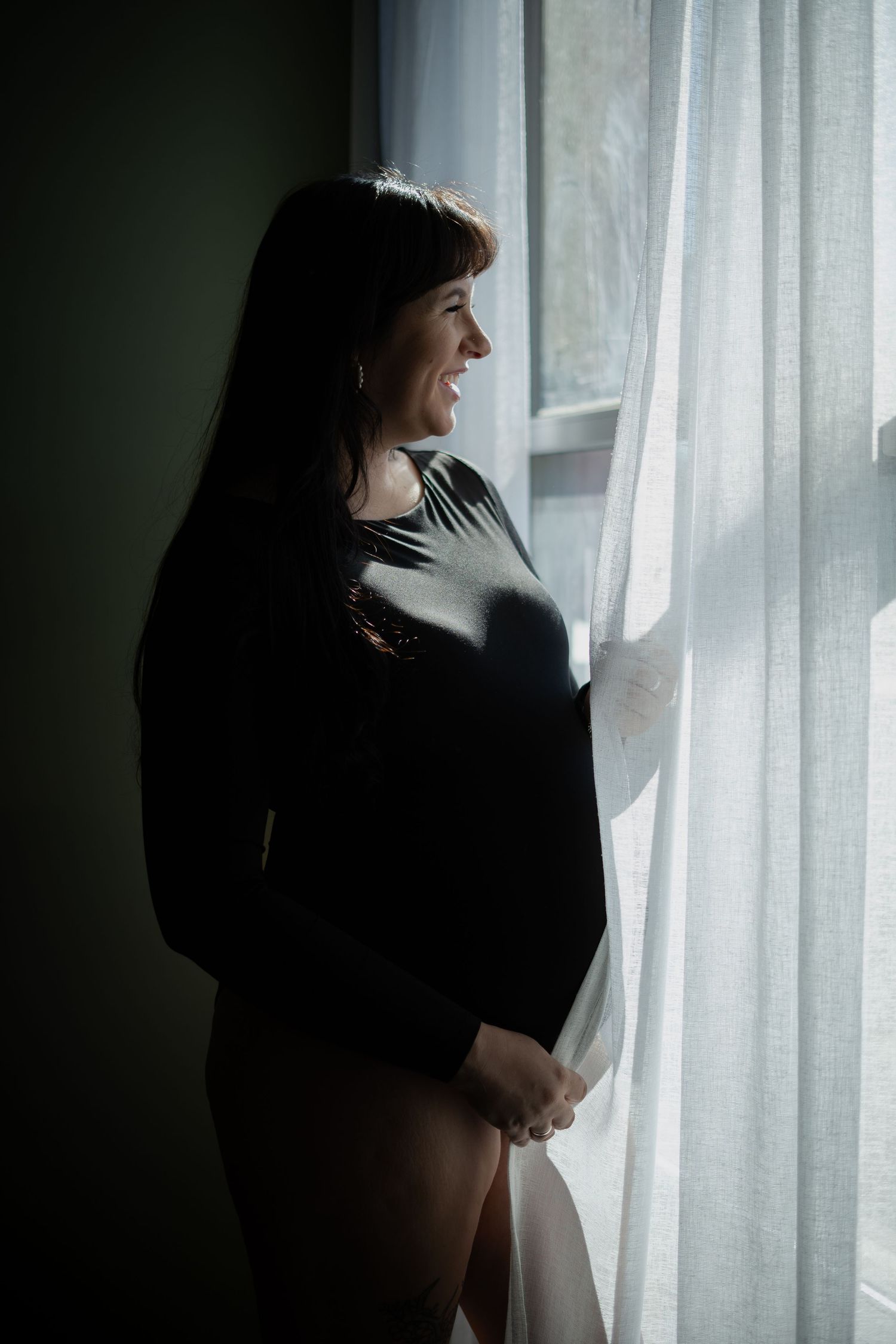 Silhouetted figure standing by sheer white curtains in moody lighting.