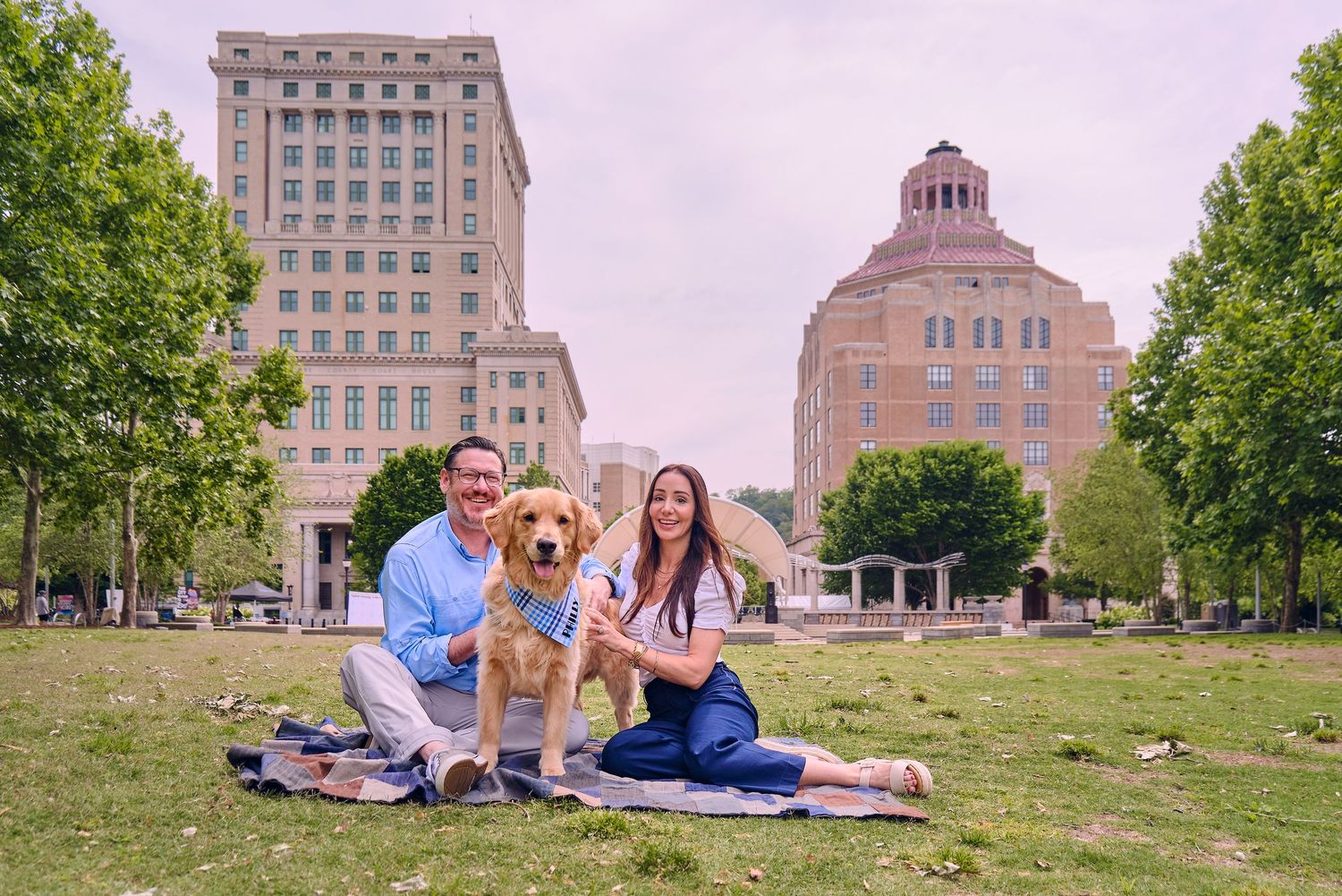 Two people walk a golden retriever at an outdoor market with a domed building visible in the background.