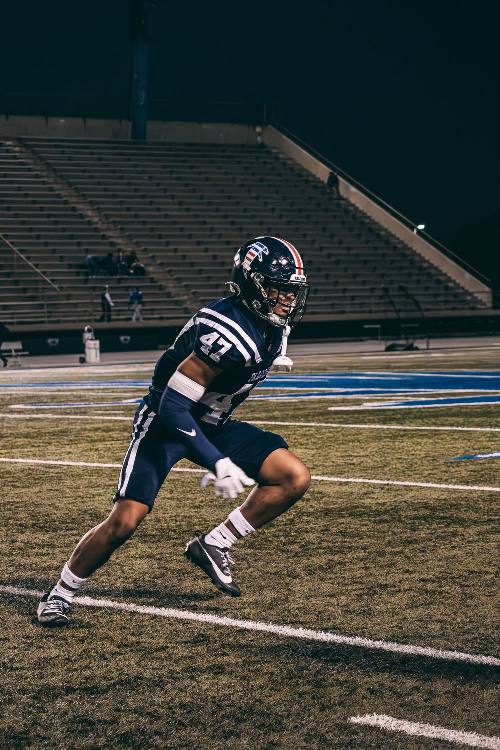 Football player in navy uniform performs agility drill on field at night.